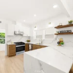 Kitchen with white cabinets, marble counter, wood shelves, and window