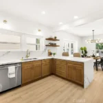 Kitchen with wood cabinets, marble counter, steel appliances, table with chairs, and big windows