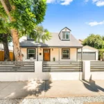 Two story California real estate house with gray roof, light walls, fence, and trees
