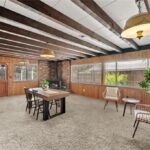 Room with wood ceiling beams, table with chairs, small plant, fireplace, carpet, and big windows