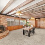 Dining area with brick fireplace, wood ceiling beams, table with chairs, and wood walls