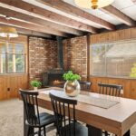 Room with wood ceiling beams, brick wall, fireplace, table with black chairs, and big windows