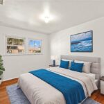 Bedroom with blue white bed, two lamps, ocean wall art, and plant by window