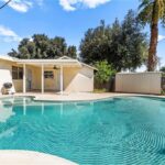California real estate home backyard with pool, grass, palm trees, and house in back