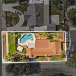 Aerial view of California home with backyard pool, green plants, and nearby homes