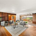 Living room with gray sofas, round coffee table, flowers, wood wall, and big windows