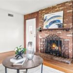 Living room with brick fireplace, wood mantle, round coffee table, wall art, and big windows