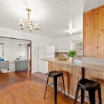 Kitchen with wood bar, two black stools, chandelier, and living room with gray sofas in back