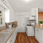 Kitchen with white cabinets, granite counter, sink by window, stove, and wood floor