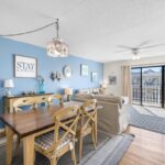 Living room with blue wall, beige sofa, wood table, big windows, wall art, and ceiling fan