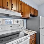 Kitchen with wood cabinets, marble counter, stove, fridge, and mirror backsplash