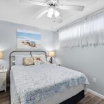 Bedroom with bed, blue quilt, beach wall art, and anchor lamps