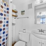 Bedroom with blue white bedspread, starfish pillow, lamps, sea wall art, and glass door to balcony