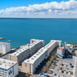 Aerial view of coastal hotel by blue bay with nearby buildings and parking