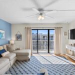 Living room with beige sofa, blue rug, blue wall, ceiling fan, and big windows to balcony