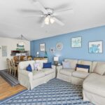 Living room with beige sofas, blue pillows, blue wall, wall art, and dining table with chairs
